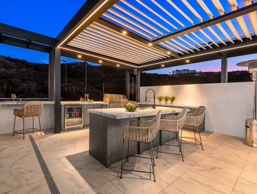 A sleek patio cover featuring a well-equipped outdoor kitchen, bar seating, and warm ambient lighting, perfect for entertaining.